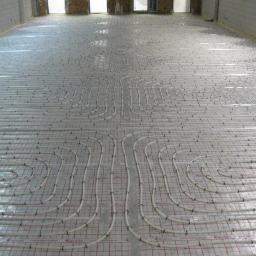 Dariusz Szaferski - Instalacje, Wykończenia i Remonty - Białe rury systemu ogrzewania podłogowego ułożone na folii z siatką w surowym wnętrzu, widok z góry.