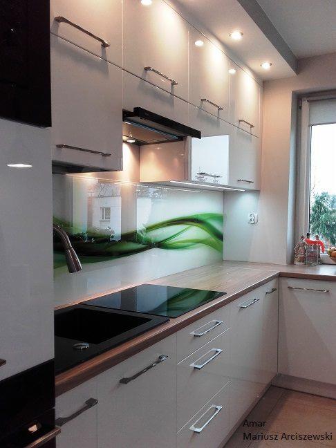 Kremowa kuchnia z drewnianym blatem, czarnym zlewem i płytą indukcyjną. Ściana zdobiona szkłem z motywem zielonych fal. Górne szafki podświetlone.