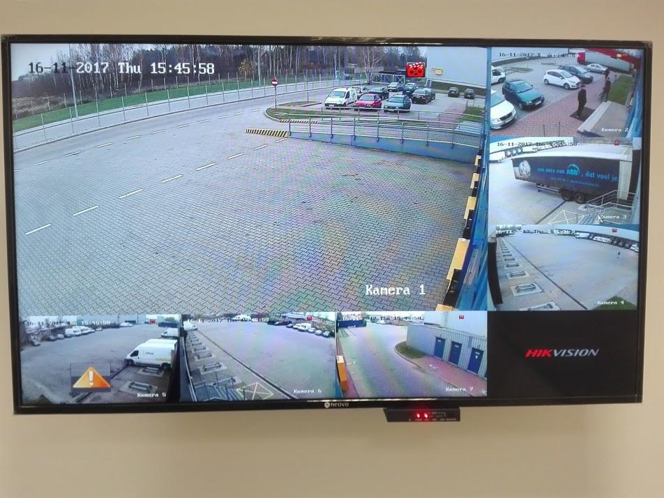 Ekran monitora z widokiem z kilku kamer monitoringu wizyjnego, pokazujący plac manewrowy, parking i fragment budynku.