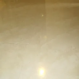 Błyszcząca, beżowa podłoga z płytek ceramicznych, widziana pod kątem, z odbiciem światła. Widoczna fuga i fragment ściany w tle.