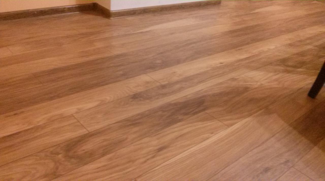 Ułożona podłoga z paneli drewnopodobnych w ciepłych odcieniach brązu, z widocznymi listwami przypodłogowymi i fragmentem nogi mebla w prawym górnym rogu.