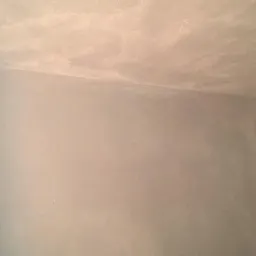 Szara ściana i sufit w rogu pomieszczenia po nałożeniu gładzi. Widoczna faktura, delikatne światłocienie. Minimalistyczny kadr ukazuje precyzję wykończenia.