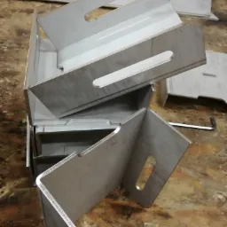 Stos metalowych, spawanych pojemników z uchwytami, ułożonych jeden na drugim na drewnianej powierzchni.