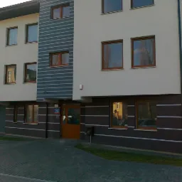 Nowoczesny budynek mieszkalny z brązowymi ramami okiennymi, balkonami z szklanymi balustradami i numerem 73 nad wejściem.