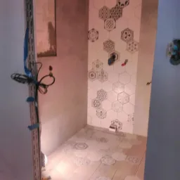 Fragment łazienki w trakcie wykańczania: ułożone heksagonalne płytki ścienne z wzorami i drewnopodobne płytki podłogowe, widoczne wystające kable i elementy instalacji.