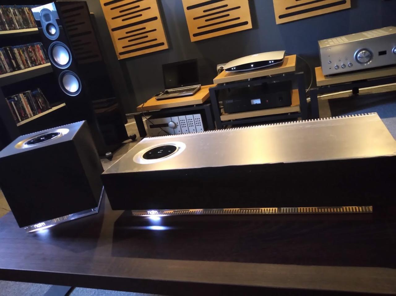 Profesjonalny system audio Naim: wzmacniacz i głośniki na drewnianym stoliku, w tle półka z płytami i panele akustyczne na ścianie.