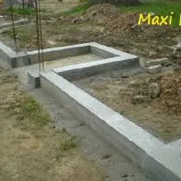 Zalane, betonowe fundamenty pod budynek, z wystającymi prętami zbrojeniowymi. Widok na zewnątrz, grunt wokół.