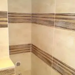 Beżowe płytki z ciemnobrązowymi pasami na ścianie w łazience, widok na narożnik kabiny prysznicowej z baterią.