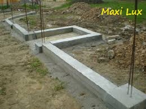 Zalane, betonowe fundamenty pod budynek, z wystającymi prętami zbrojeniowymi. Widok na zewnątrz, grunt wokół.