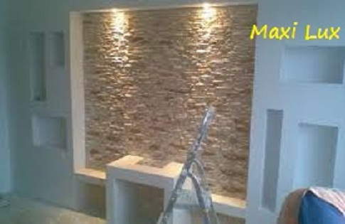 Dekoracyjna ściana z kamienia podświetlona punktowo, z widoczną drabiną, sugerująca prace wykończeniowe w nowoczesnym wnętrzu. Elementy dekoracyjne na ścianie.