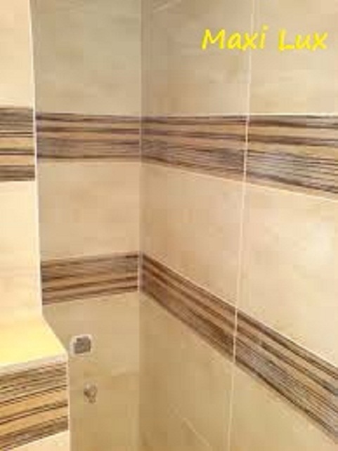 Beżowe płytki z ciemnobrązowymi pasami na ścianie w łazience, widok na narożnik kabiny prysznicowej z baterią.