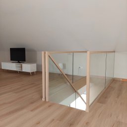 Schody Drewniane Bartosz Paczkowski - Nowoczesna balustrada szklana z drewnianymi słupkami na antresoli, widok na schody i salon z telewizorem.