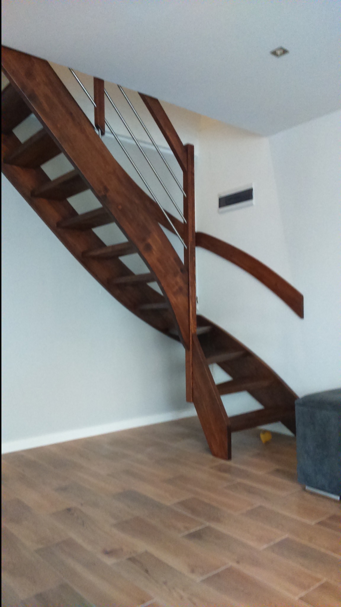 Drewniane schody gięte z metalową balustradą w nowoczesnym wnętrzu, widok z dołu na jasną podłogę.