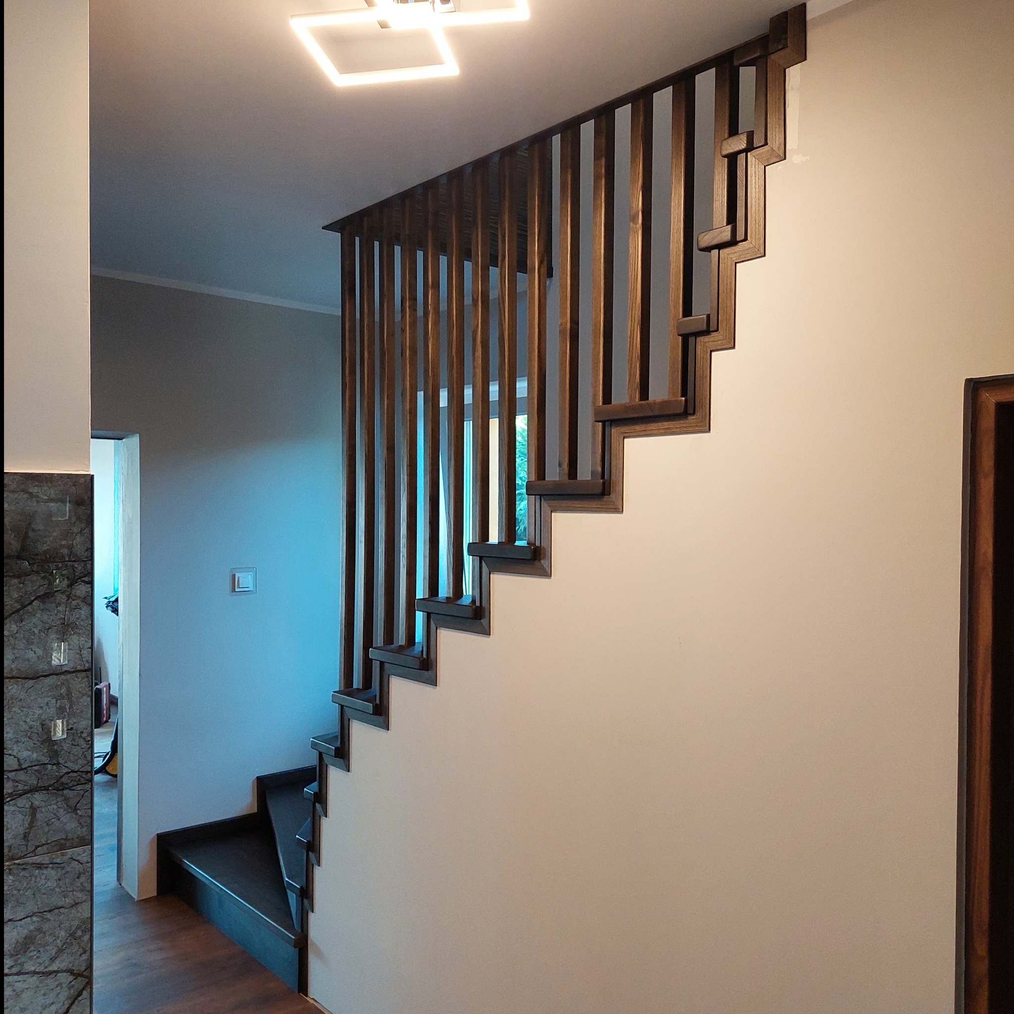 Nowoczesne schody z ciemnego drewna z pionową balustradą, widok z dołu, oświetlenie sufitowe LED.