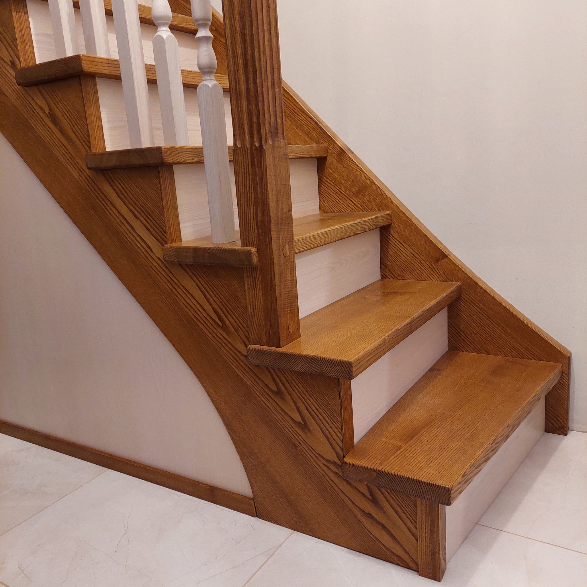 Fragment nowoczesnych schodów drewnianych z jasnymi podstopnicami i balustradą z białymi tralkami. Widoczne detale wykończenia i struktura drewna.