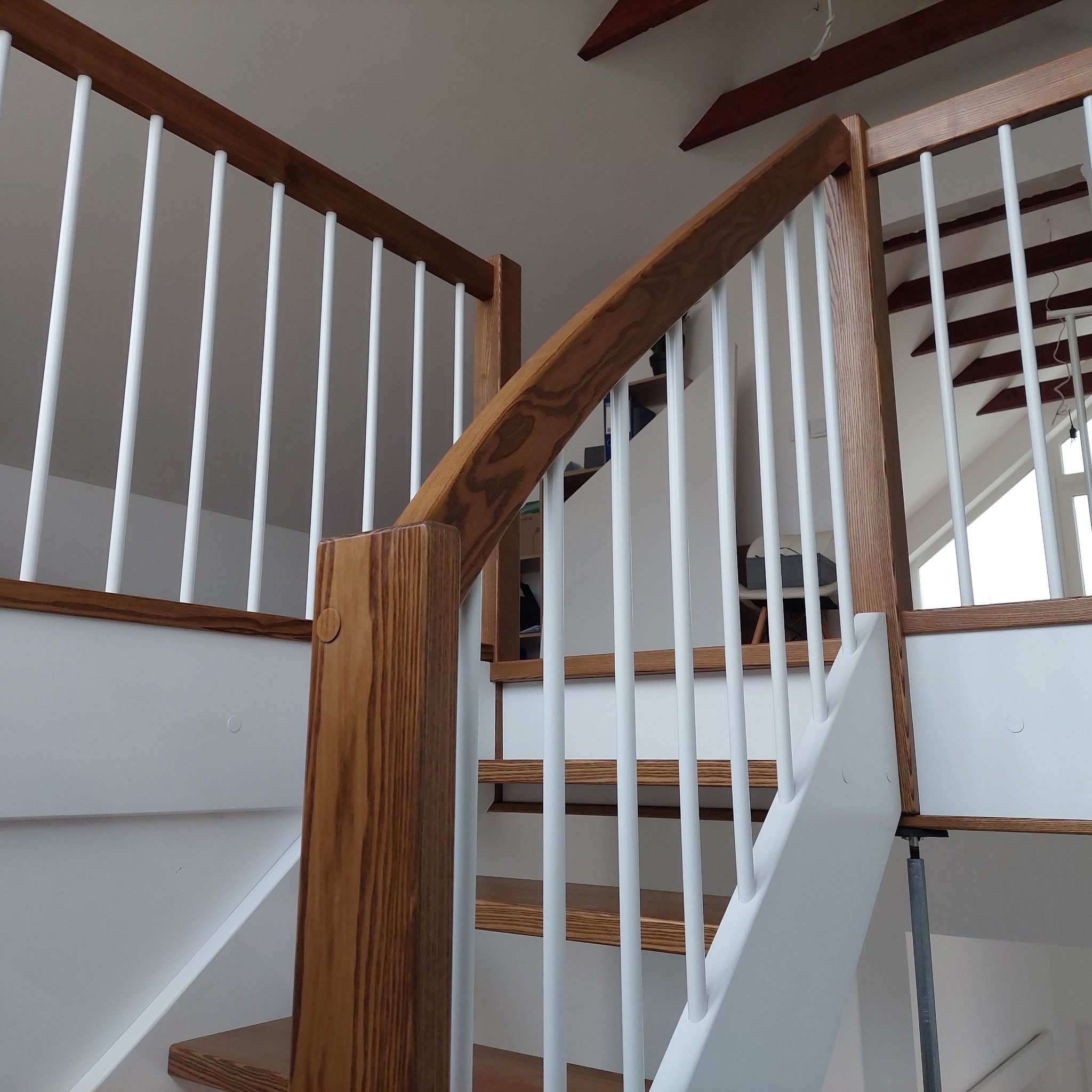 Drewniane schody z białą balustradą sztabową w domu w Trzemesznie. Widok z dołu, z widocznymi elementami konstrukcyjnymi i wykończeniowymi.