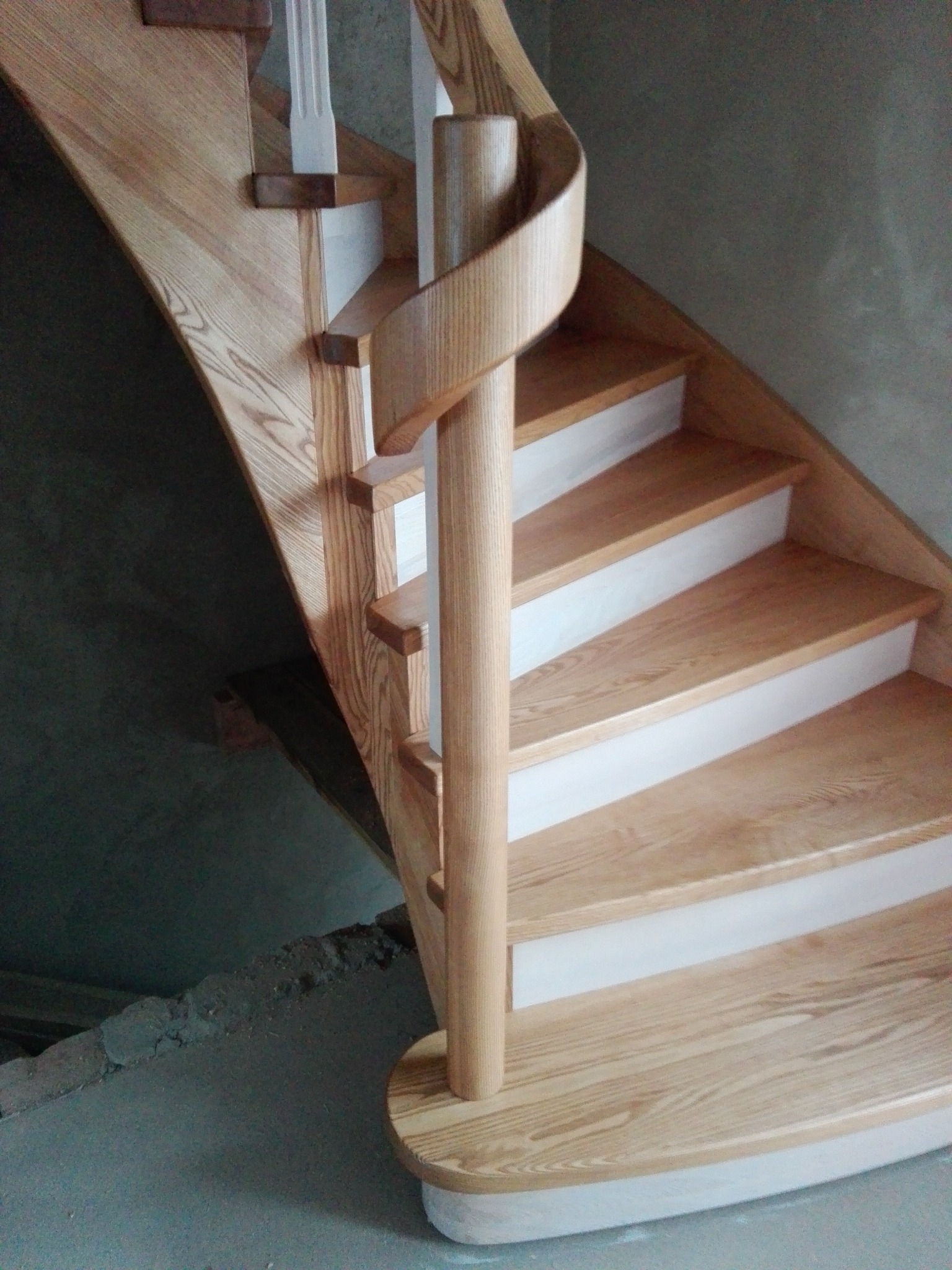 Kręte schody z jasnego drewna z białą podbitką, wykonane w Trzemesznie. Spiralna poręcz i widoczne usłojenie drewna dodają elegancji.