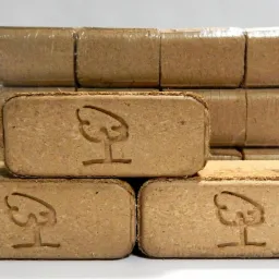 Ułożone brykiety drzewne z wytłoczonym symbolem drzewa, zapakowane w folię.