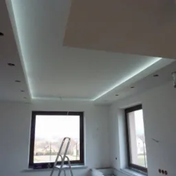 Wykończone wnętrze z podwieszanym sufitem z oświetleniem LED i otworami na halogeny, widoczne okna i drabina w pomieszczeniu.