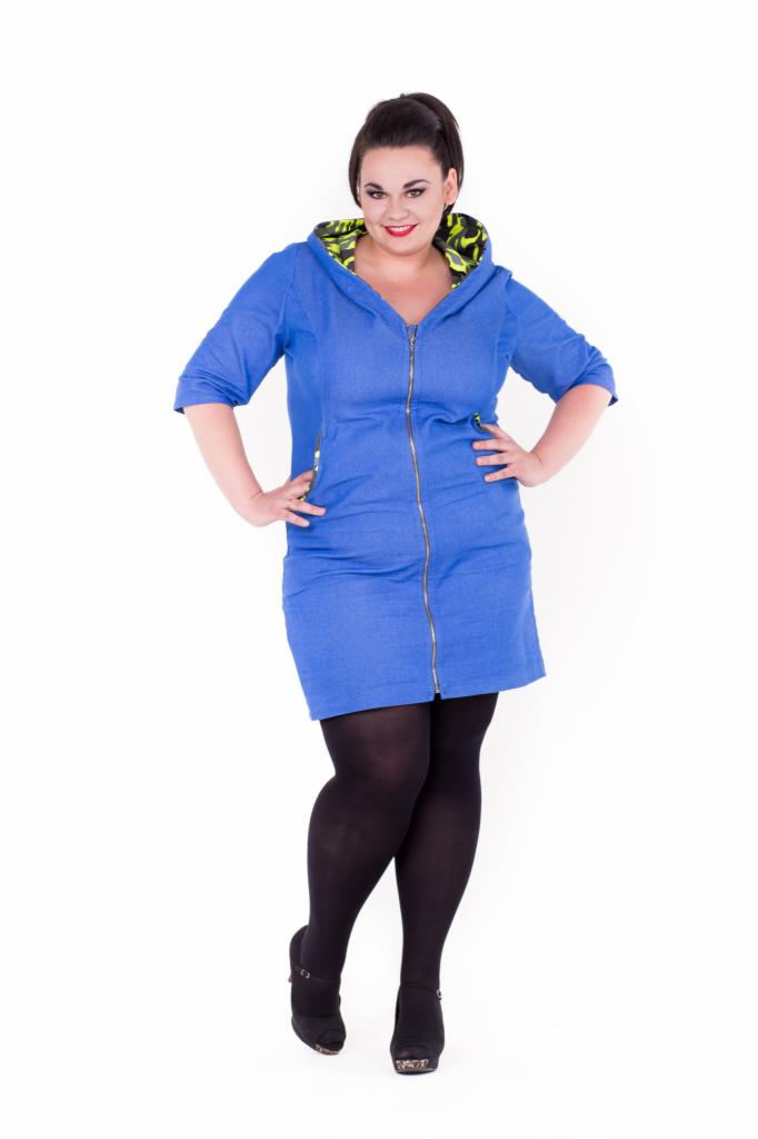 Kobieta w niebieskiej sukience dresowej z kapturem wykończonym wzorzystą podszewką, czarnych rajstopach i botkach na platformie, pozująca na białym tle.