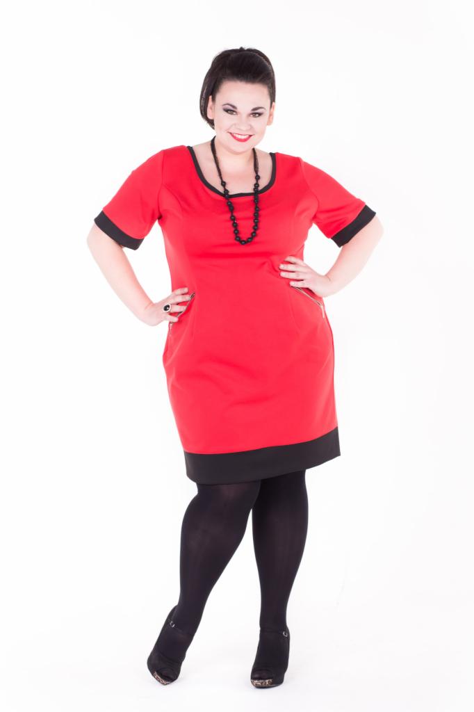 Kobieta w czerwonej sukience z czarnymi wstawkami i rajstopach pozuje na białym tle, prezentując kreację.