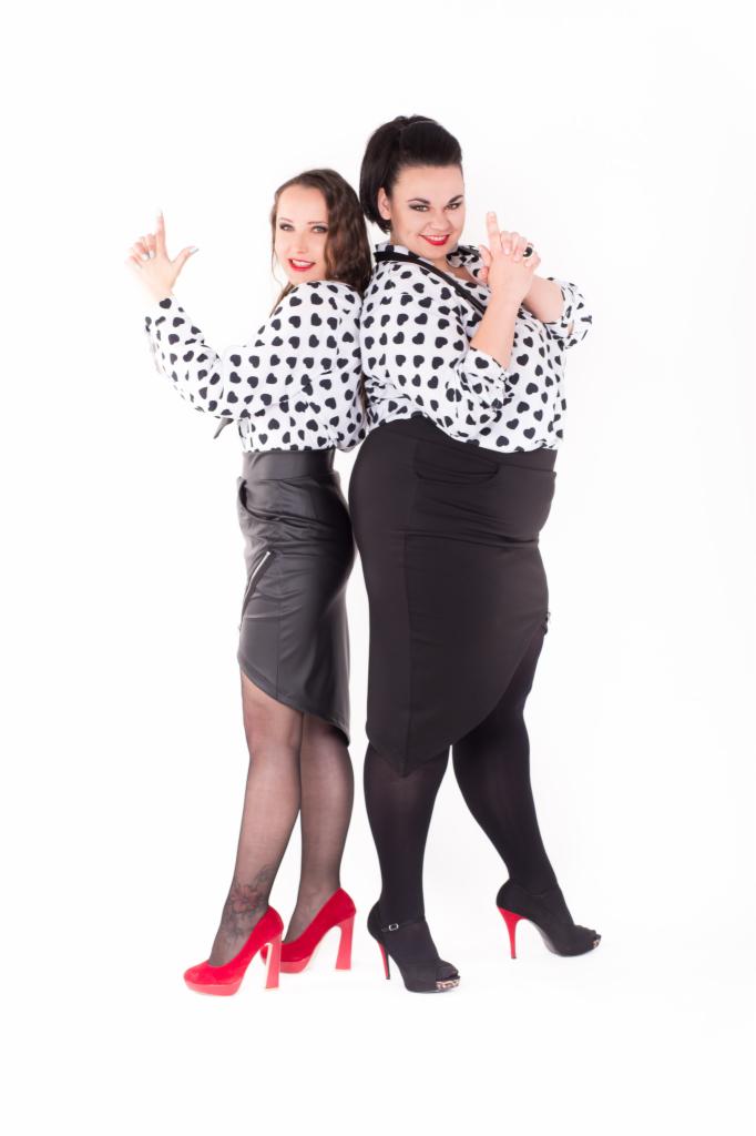 Dwie kobiety w stylizowanych strojach: bluzki w czarne serca, czarna skórzana spódnica z asymetrycznym dołem i czerwone szpilki oraz czarna spódnica ołówkowa i czarne szpilki z czerwonymi obcasami,...