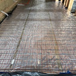 Comfort System House Tomasz Pawłowski - Rozłożona mata grzewcza na folii z siatką, przygotowana do zalania wylewką, widoczne kable zasilające, ocieplenie stropu wełną mineralną.