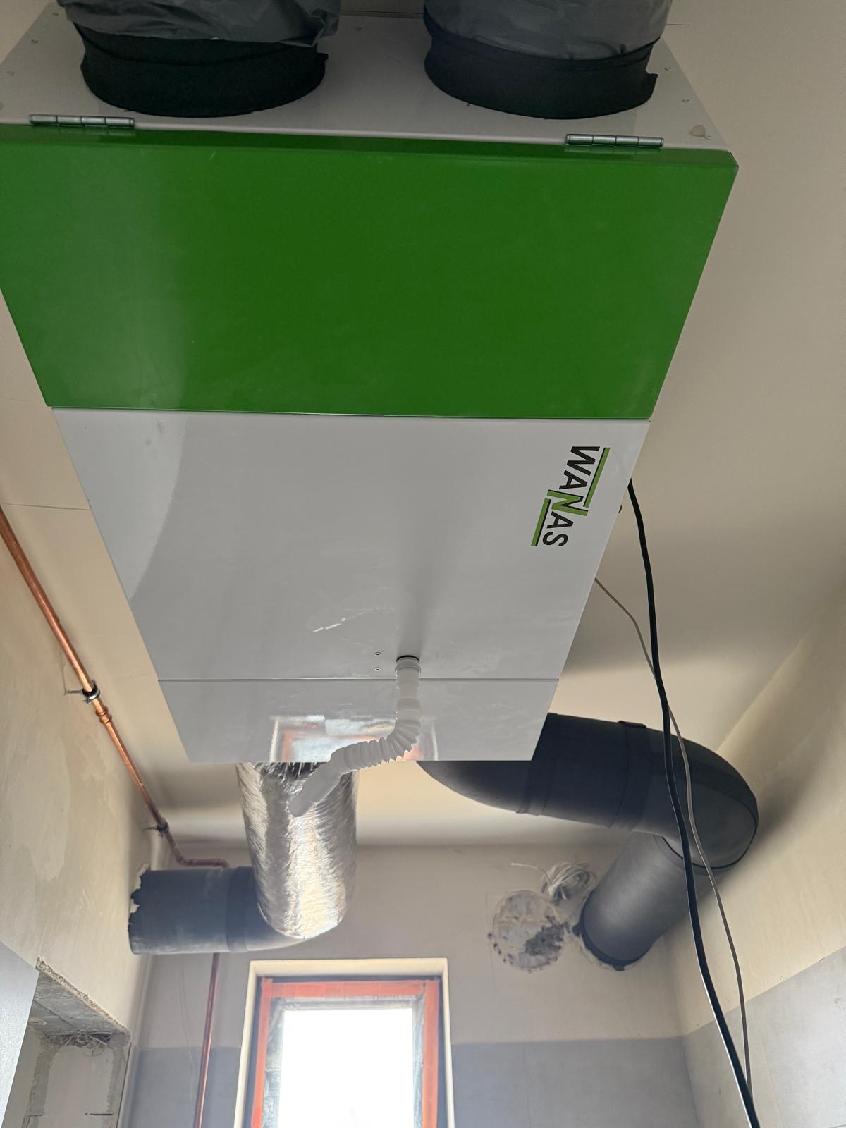 Centrala wentylacyjna z rekuperacją marki WANAS, widoczne podłączenia przewodów wentylacyjnych w surowym wnętrzu.