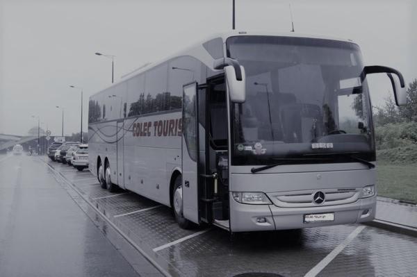 Szary autokar turystyczny z otwartymi drzwiami stoi na mokrym parkingu, widoczne logo firmy 'GOLEC TOURIST'.