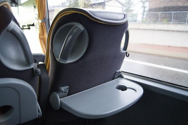 Wnętrze autobusu: szare siedzenie z rozkładanym stolikiem przy oknie, widok na mokrą ulicę.