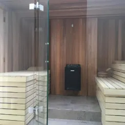 Wnętrze sauny wykończonej drewnem, z piecem marki Harvia i szklanymi drzwiami, zrealizowanej w Knybawie.