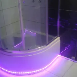 Nowoczesna kabina prysznicowa z podświetleniem LED w odcieniach fioletu, czarne płytki z wzorem, białe fugi. Ujęcie z bliska, widoczne detale wykończenia.