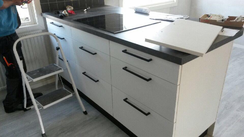Montaż blatu kuchennego z płytą indukcyjną i białymi szafkami z czarnymi uchwytami, widoczna drabina i narzędzia.