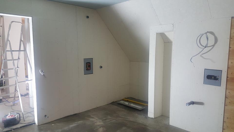 Wnętrze poddasza w trakcie prac wykończeniowych we Wrocławiu, ściany pokryte płytami gipsowo-kartonowymi, widoczne instalacje elektryczne i hydrauliczne, drabina oraz narzędzia.