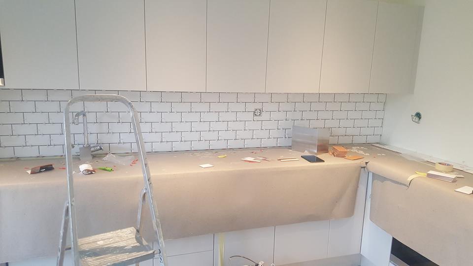 Montaż białych płytek typu metro w kuchni, zabezpieczony blat, drabina oparta o ścianę, widoczne narzędzia i akcesoria glazurnicze.