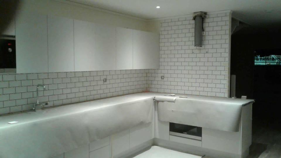 Wnętrze kuchni w trakcie remontu: białe szafki wiszące, ściana wyłożona białymi płytkami typu metro, blat zabezpieczony folią ochronną, widoczny fragment instalacji wentylacyjnej.