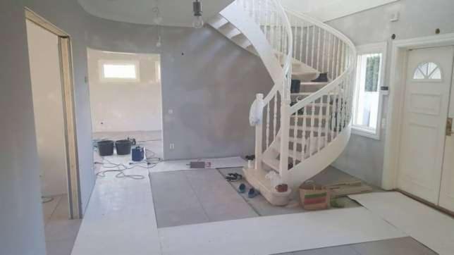 Wnętrze w trakcie remontu: spiralne schody, ściana przygotowana do malowania, zabezpieczona podłoga, widoczne narzędzia i akcesoria malarskie.