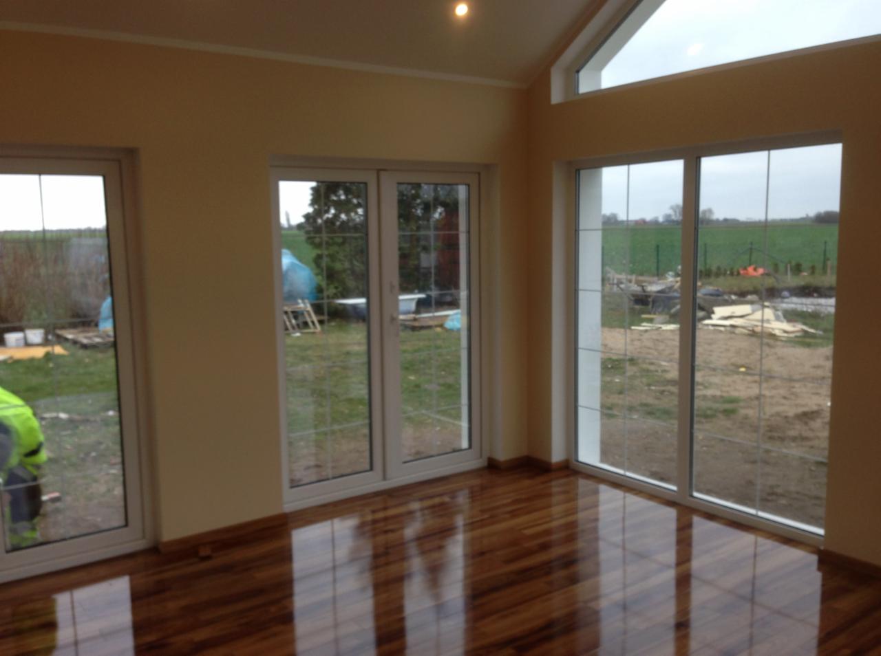 Nowoczesne wnętrze z drewnianą podłogą i dużymi oknami we Wrocławiu, widok na ogród z elementami placu budowy.