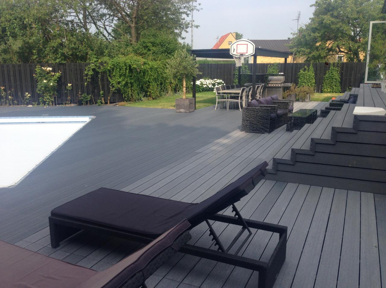 Kompozytowy taras w odcieniach szarości z leżakami, schodami i meblami ogrodowymi, widok na basen i kosz do koszykówki.