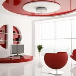 Nowoczesne wnętrze: białe ściany, czerwone akcenty, okrągłe półki, designerskie krzesła i sufit z nietypowym oświetleniem. Minimalistyczny styl i jasne, przestronne pomieszczenie.