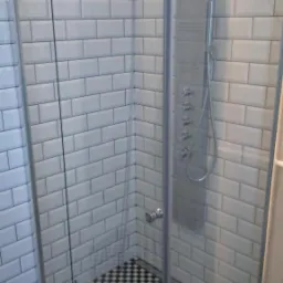 Nowoczesna kabina prysznicowa z deszczownicą i panelem natryskowym, wykończona białymi płytkami typu metro i czarno-białą szachownicą na podłodze.