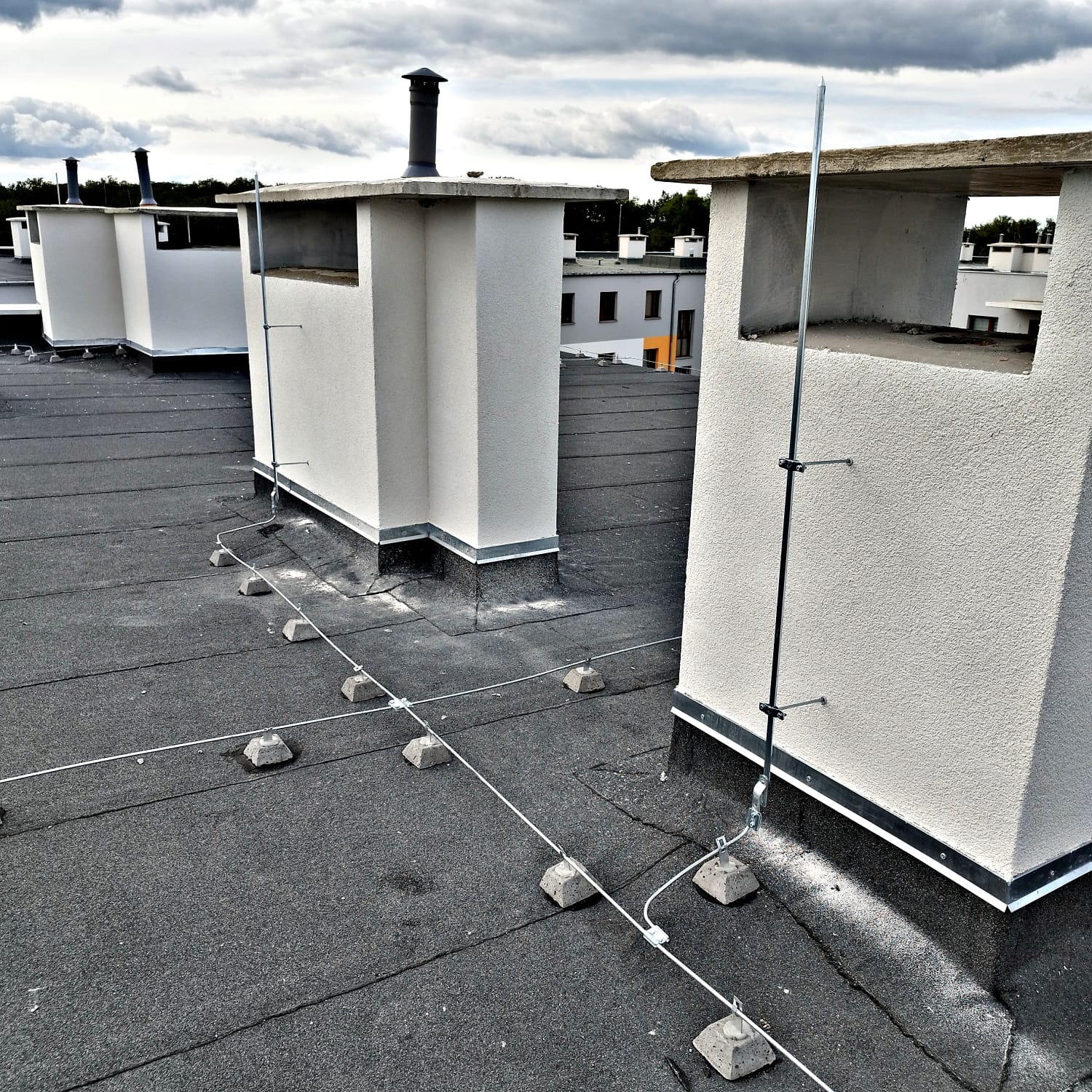 Instalacja odgromowa na dachu budynku w Gorzowie Wielkopolskim. Widoczne przewody i maszty odgromowe przy kominach na tle pochmurnego nieba.