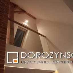 Wnętrze z ceglanym kominem i drewnianą konstrukcją dachu we Wrocławiu. Minimalistyczny design z oknem dachowym i subtelnym oświetleniem.