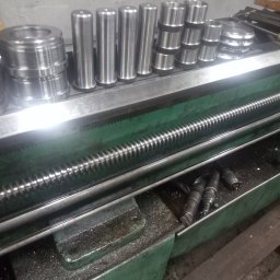 USŁUGI TOKARSKO-ŚLUSARSKIE ARIEL SKUCZYŃSKI - Metalowe elementy o różnych kształtach ułożone na zielonej tokarce, widoczne wióry i narzędzia.