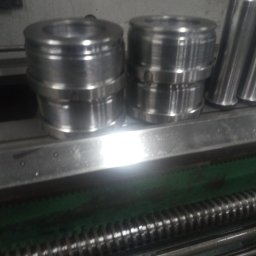 USŁUGI TOKARSKO-ŚLUSARSKIE ARIEL SKUCZYŃSKI - Dwa metalowe elementy cylindryczne z obróbki skrawaniem, leżące na metalowej powierzchni tokarki z widoczną śrubą pociągową.