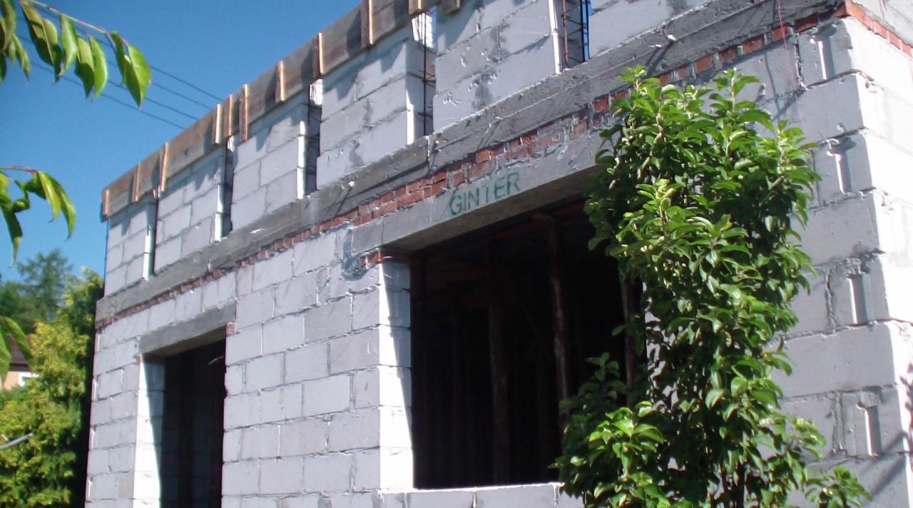 Surowy stan budynku w trakcie murowania ścian z betonu komórkowego. Widoczne otwory okienne i zbrojenia. Na murze napis 'GINTER'.