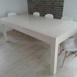 Stolarnia Solarscy - Jasny, prostokątny stół z drewna z szufladą, otoczony białymi krzesłami na drewnianych nogach, na tle ściany z cegły w nowoczesnej jadalni.