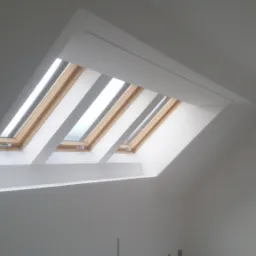 Poddasze po remoncie z trzema oknami dachowymi w drewnianej ramie, pomalowanymi na biało wnękami i ścianami, oraz dodatkowym oknem pionowym z widokiem na las.