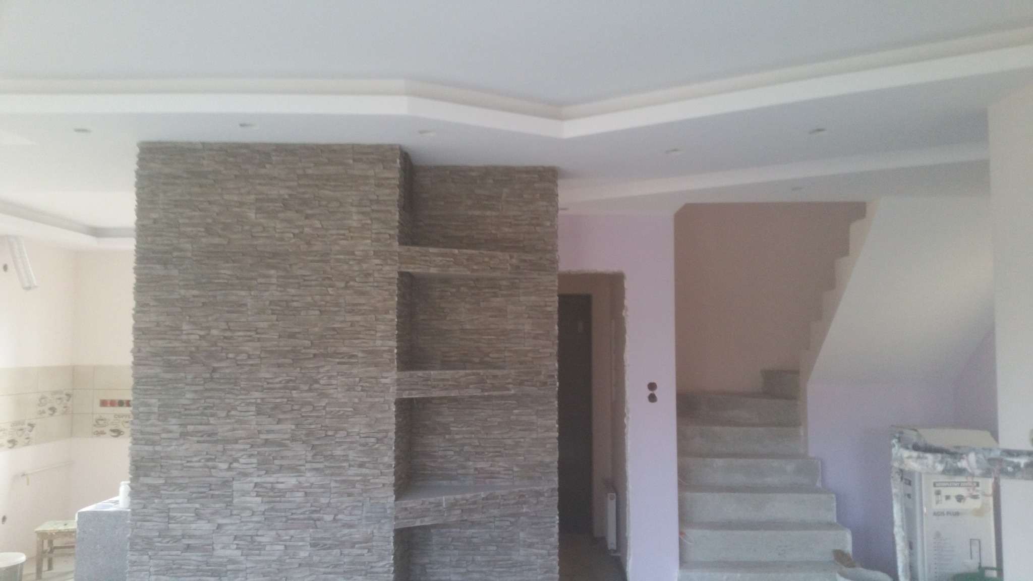 Ściana działowa z dekoracyjnej cegły z wnękami w surowym stanie, widoczne schody w tle, częściowo wykończone wnętrze.