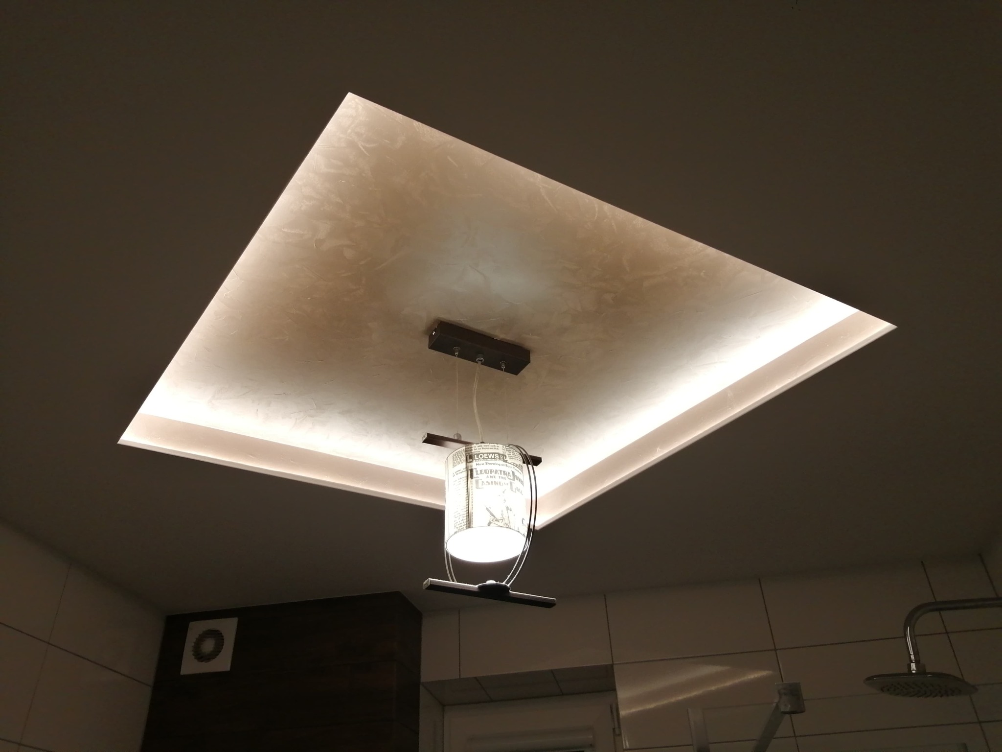 Kwadratowy sufit podwieszany z oświetleniem LED i dekoracyjną fakturą, z wiszącą lampą z abażurem w stylu retro, widok z dołu w łazience.